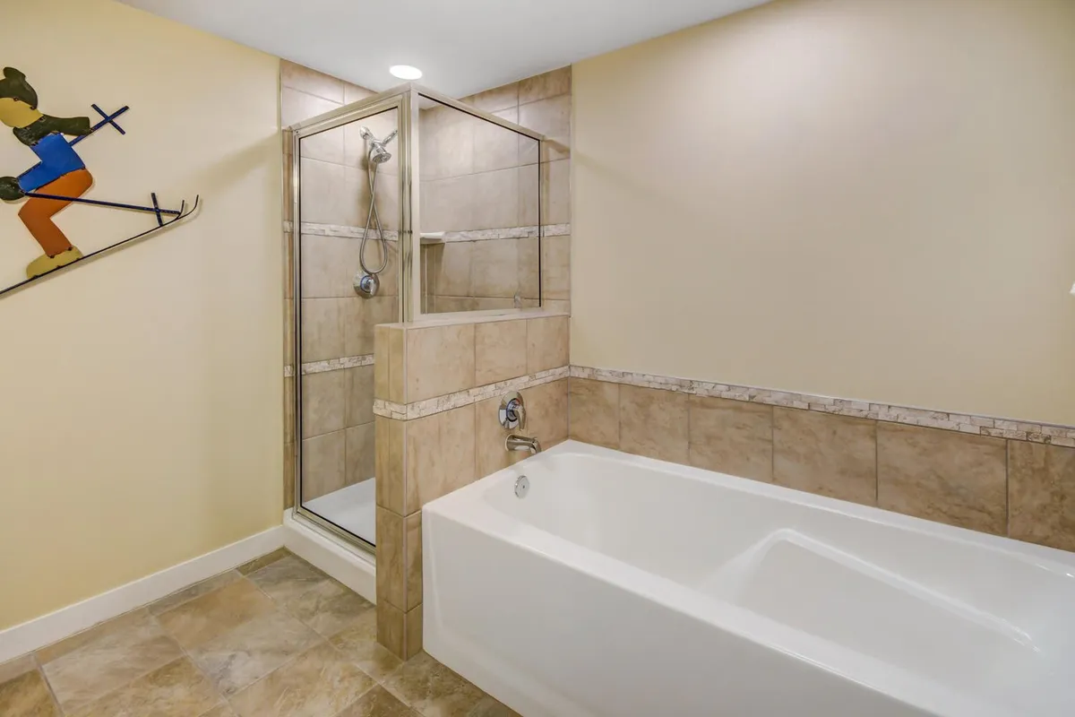A serene bathroom featuring a bathtub and a shower enclosure, accented with playful skiing decor. The space is designed for relaxation after a day of mountain adventures.