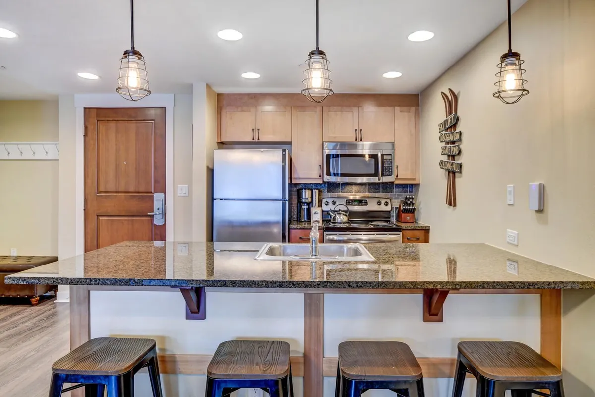 This image spotlights a sleek, modern kitchen with granite countertops, stainless steel appliances, and warm pendant lighting. The countertop is central to the scene, suggesting a space perfect for both prep work and gathering. The overall mood is cozy and modern, inviting guests to cook or socialize in style.