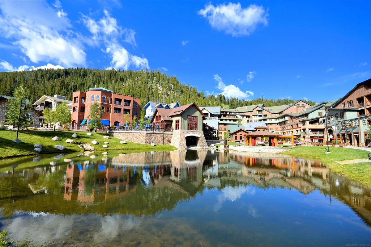 An inviting exterior view of a pond surrounded by colorful buildings and a charming bridge. The area is lively, suggesting opportunities for walking, picnicking, and community events.