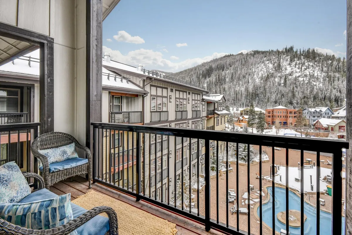 A private deck with comfortable seating overlooks snow-covered mountains and a serene winter landscape. The tranquil setting is perfect for sipping gourmet coffee while enjoying village and ski run views, extending the gathering space outdoors.