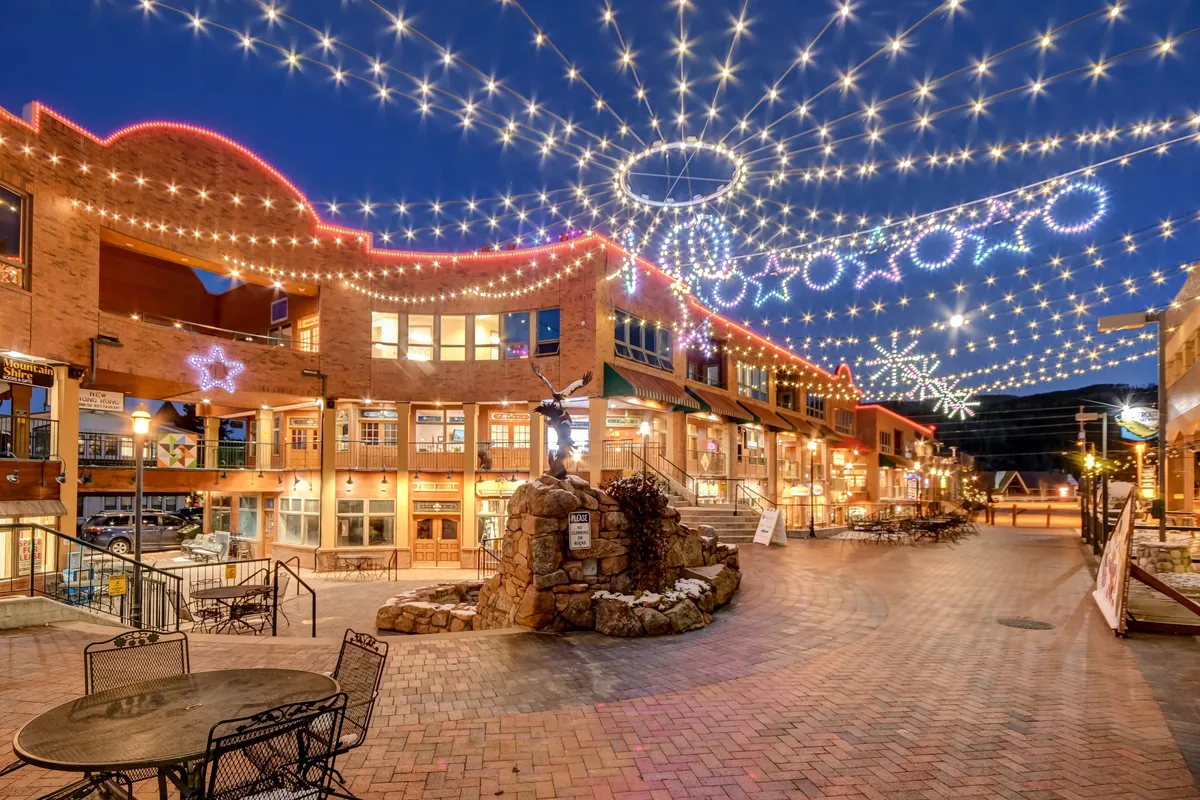 This exterior image showcases a lively outdoor plaza adorned with festive string lights and decorative star ornaments. A stone fountain serves as a central focal point, and the scene hints at various activities such as shopping, dining, and socializing, with an inviting, joyful atmosphere ideal for community gatherings and seasonal events.
