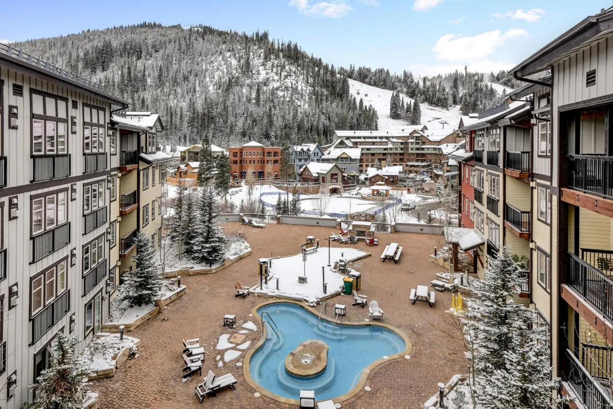 A tranquil but inviting exterior shot showing a steaming outdoor pool framed by snow, with surrounding resort buildings and the winter landscape visible in the background. The scene evokes relaxation and après-ski enjoyment, suggesting amenities like the massive hot tub mentioned in the section.