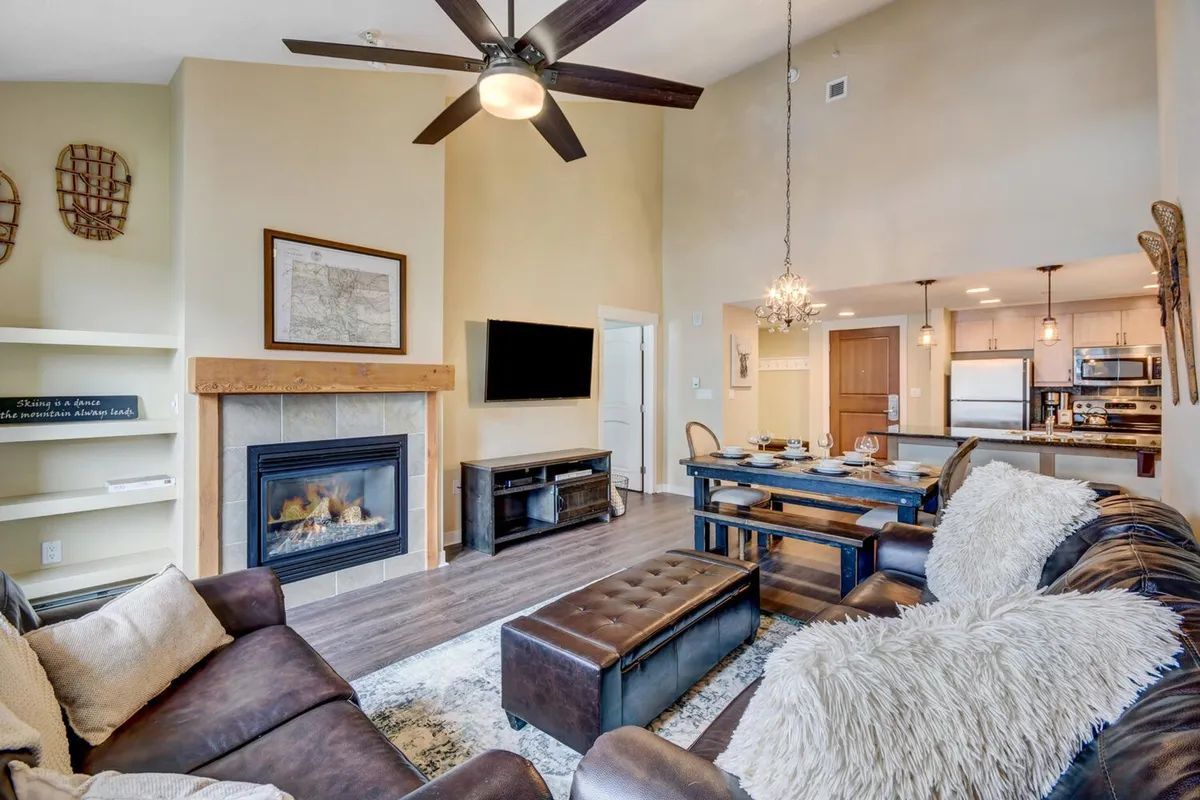An open-concept living and dining space with a rustic-chic fireplace, a welcoming dining table, and a plush sofa. The chandelier and decor add a touch of mountain charm, while the layout encourages relaxed group gatherings and shared activities.